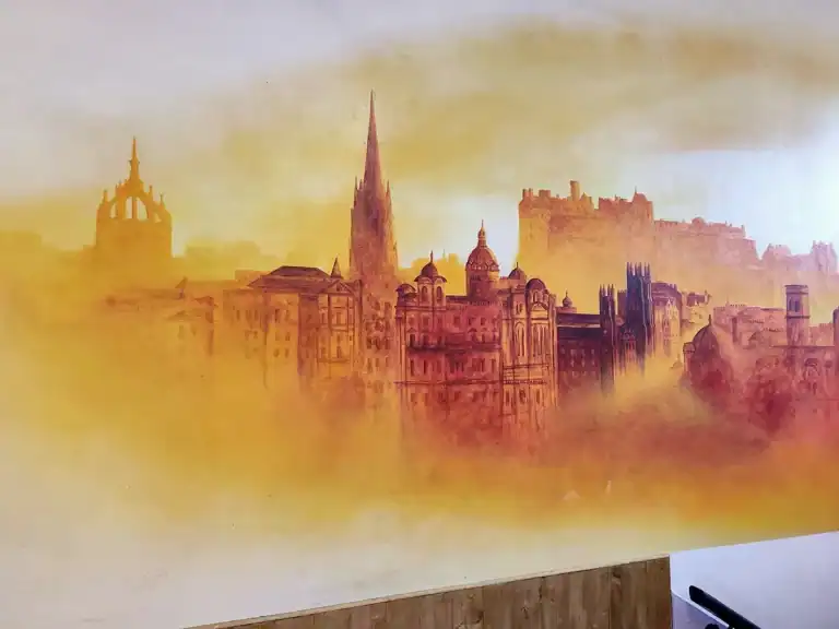 Art in a wall of a cafe by mural painter David Jimenez of the Edinburgh skyline in orange tones.